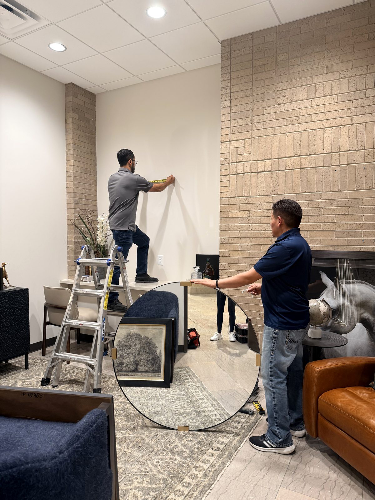 Two crew members measuring a wall and holding a round mirror during an installation