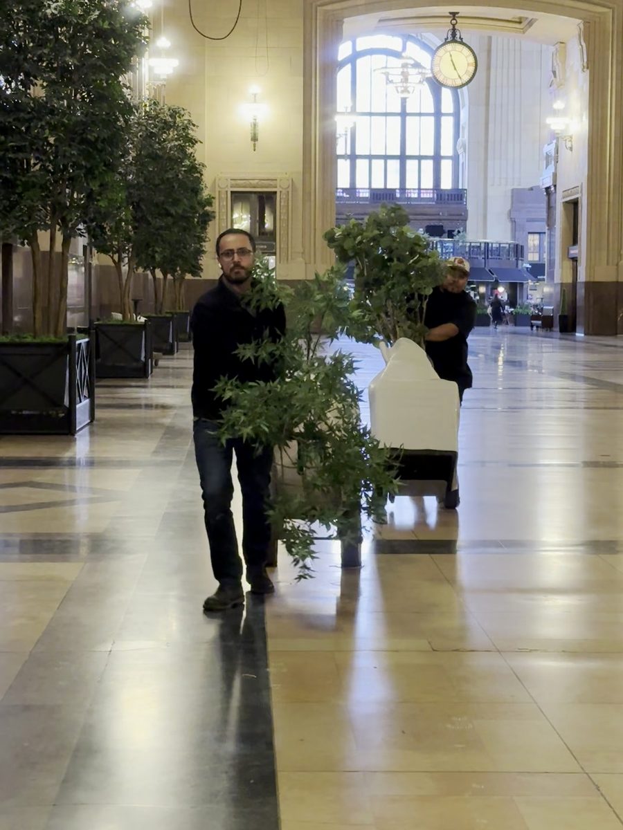 Two crew members moving a wrapped sofa on a dolly through a grand hall on an install day